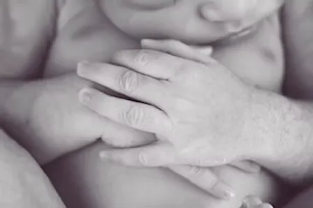 Parent's hands cradling tiny newborn hands